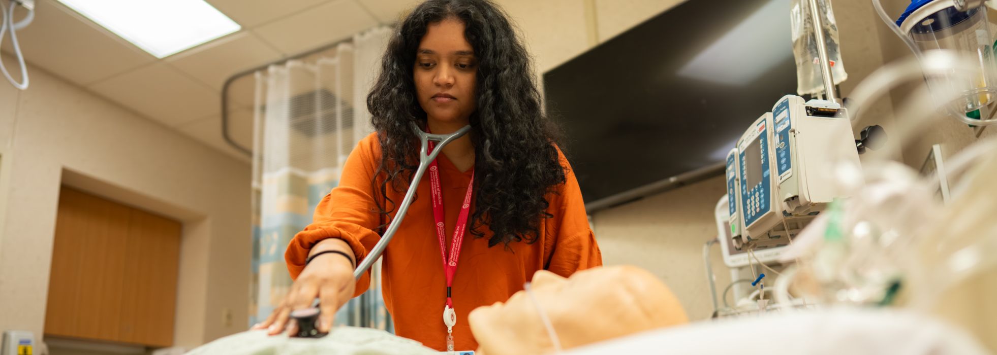 A resident in the simulation center with a stethoscope pressed to a mannequin