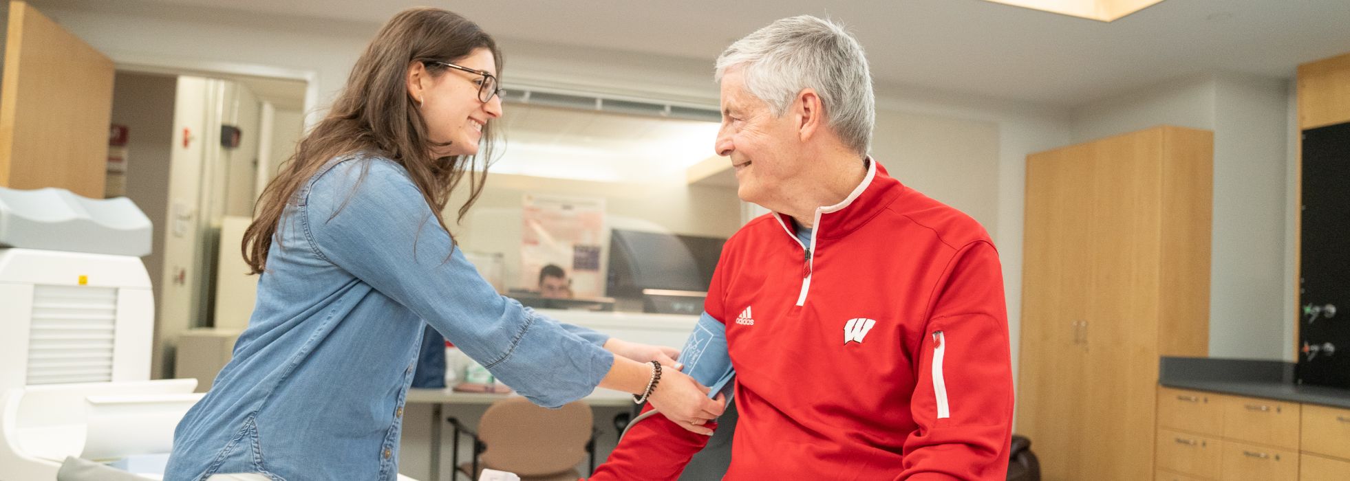 A woman adjusts a blood pressure cuff on a man with gray hair