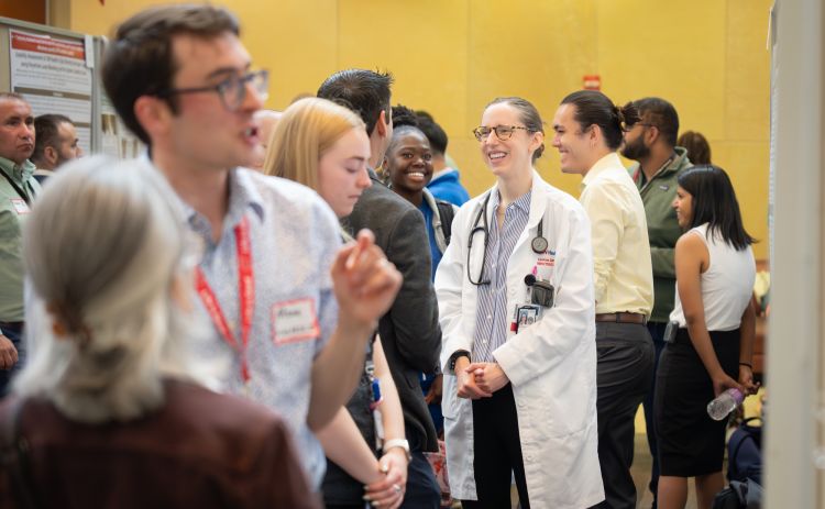 Michael Scolarici, MD, in light blue, and Caroline Ewing, MD, in white coat at center, both fellows in the Division of Infectious Disease, share their research at the poster session.