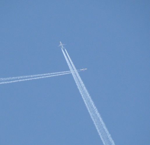 Two jet flying through a blue sky with their contrails crossing.