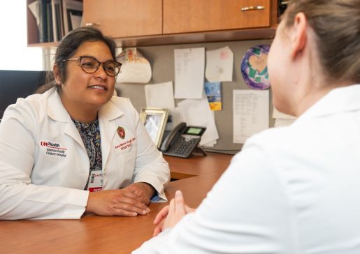 Dr. Singh wearing a lab coat and talking to a fellow across a desk