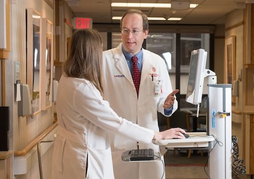 Dr. Didier Mandelbrot talks with a colleague by a computer in the hallway of University Hospital