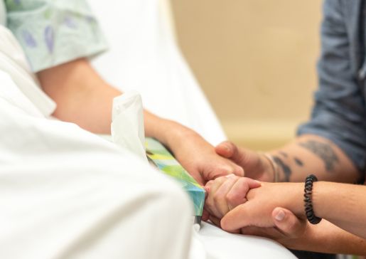 Patient in hospital bed, holding hands with loved ones.